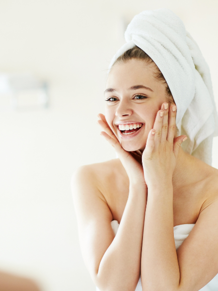A woman smiling and enjoying her skincare